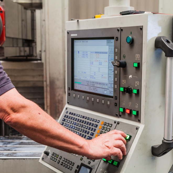 Überbrückungshilfe Corona (im Bild: Mitarbeiter bedient in einer Produktionshalle eine Maschine)
